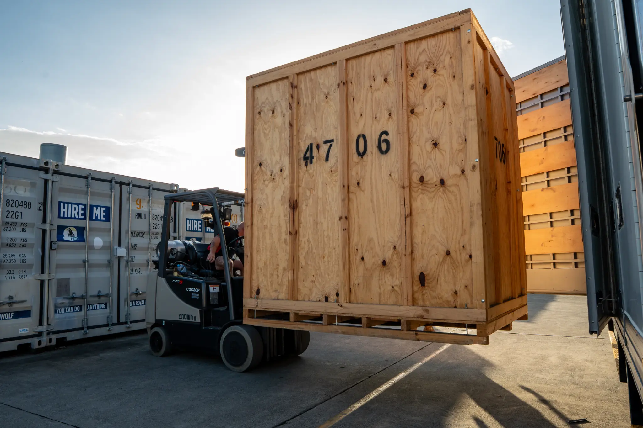 A forklift carrying a full timber storage module to a transport truck